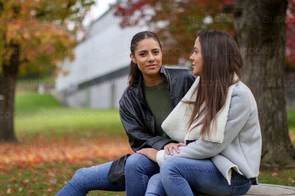 Young lesbian couple sitting outdoors in autumn - Australian Stock Image