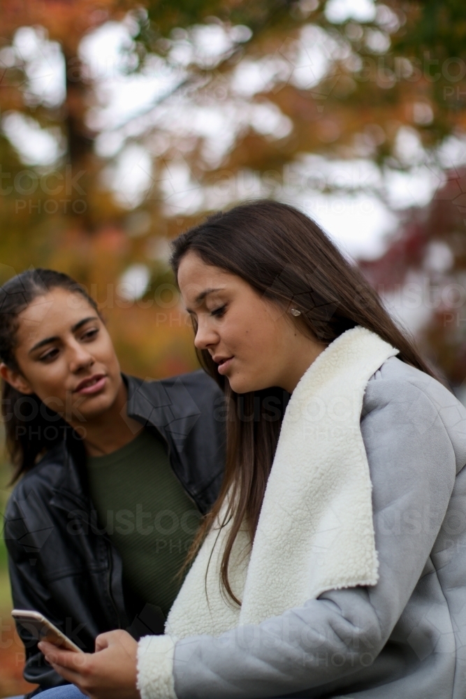 Young lesbian couple talking distracted by phone - Australian Stock Image