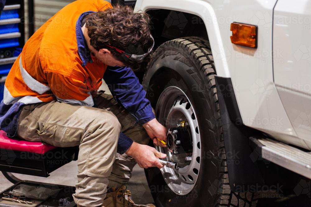 Young male mechanic adjusting the lug nuts on the wheel of white utility vehicle - Australian Stock Image