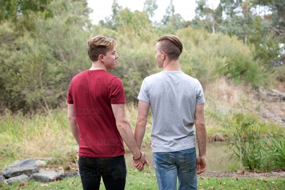Young male same sex couple holding hands in a rural setting - Australian Stock Image
