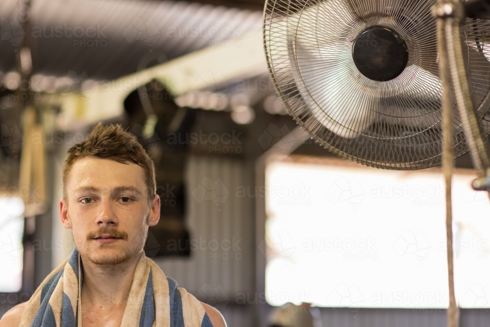 young male shearer with towel draped around neck enjoying cool air from fan - Australian Stock Image