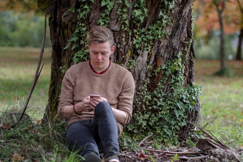 Young male sitting outside using mobile phone - Australian Stock Image