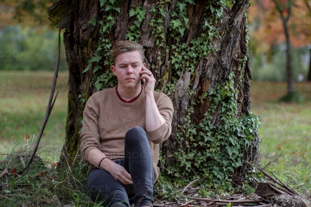 Young male sitting outside using mobile phone - Australian Stock Image