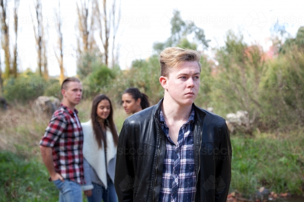 Young male standing in front of a group of young people talking in an outdoor setting - Australian Stock Image