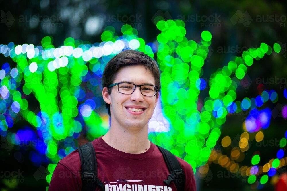 Young male uni student grinning with backdrop of holiday Christmas lights - Australian Stock Image