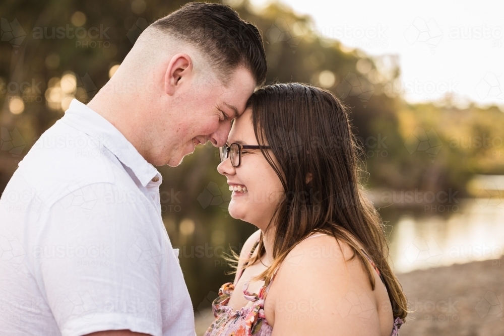 Young man and woman boyfriend and girlfriend foreheads touching laughing with water in background - Australian Stock Image