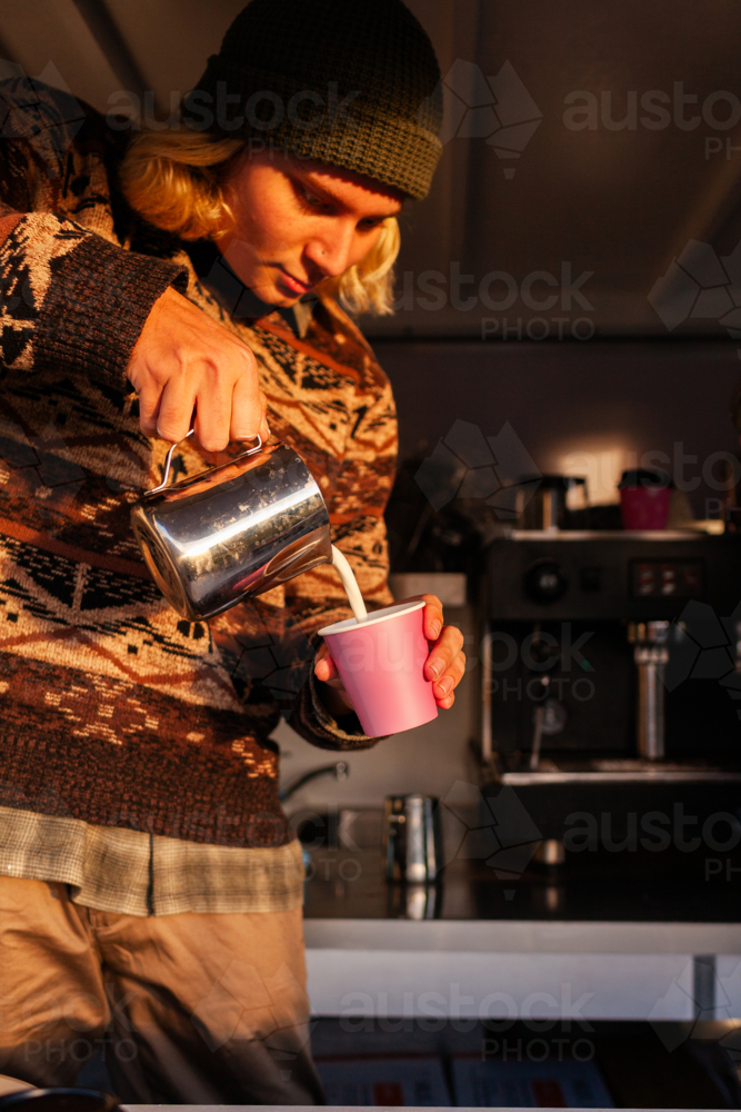Young man barista pouring milk while making a hot coffee in mobile van - Australian Stock Image