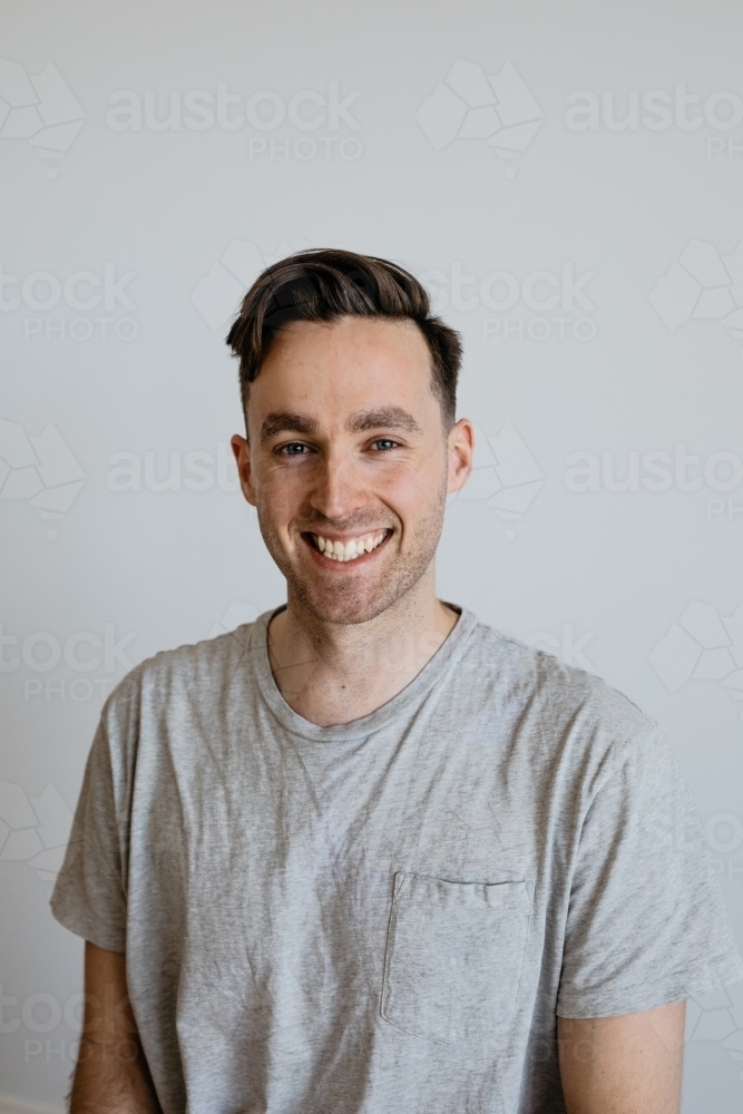 Young man big smile grey shirt plain background - Australian Stock Image