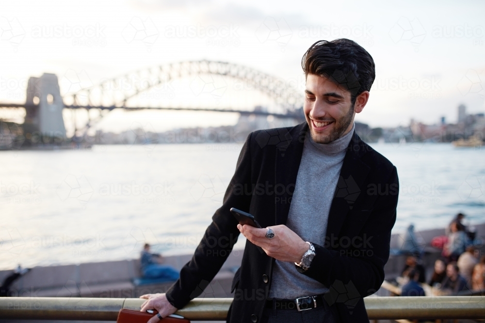 Young man checking message in front of Sydney Harbour Bridge - Australian Stock Image