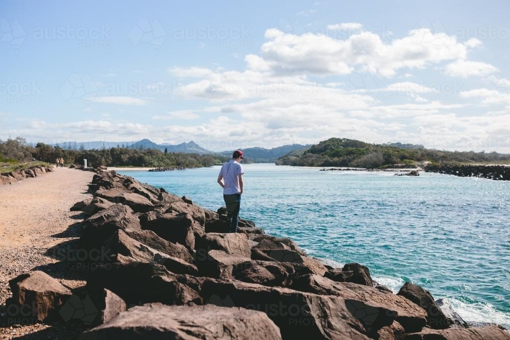 Young man climbing down rock wall towards the ocean - Australian Stock Image