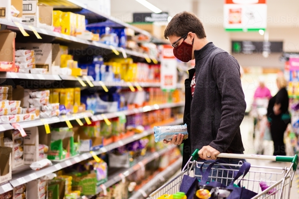 Young man doing grocery shopping for family during coronavirus outbreak wearing a face mask - Australian Stock Image