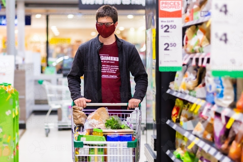 Young man doing grocery shopping for family during coronavirus outbreak wearing a face mask - Australian Stock Image
