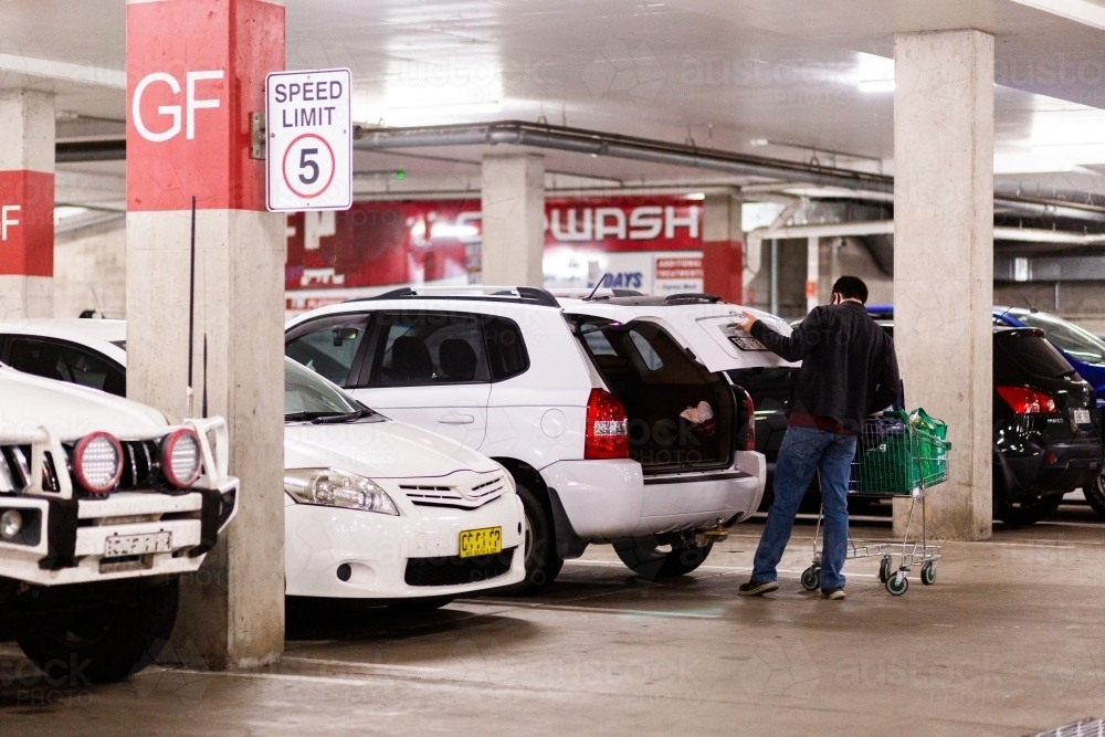 Young man doing the shopping and taking re-usable bags of groceries to the car - Australian Stock Image