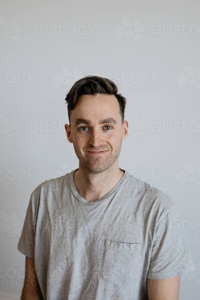 Young man dorky smile grey shirt plain background - Australian Stock Image