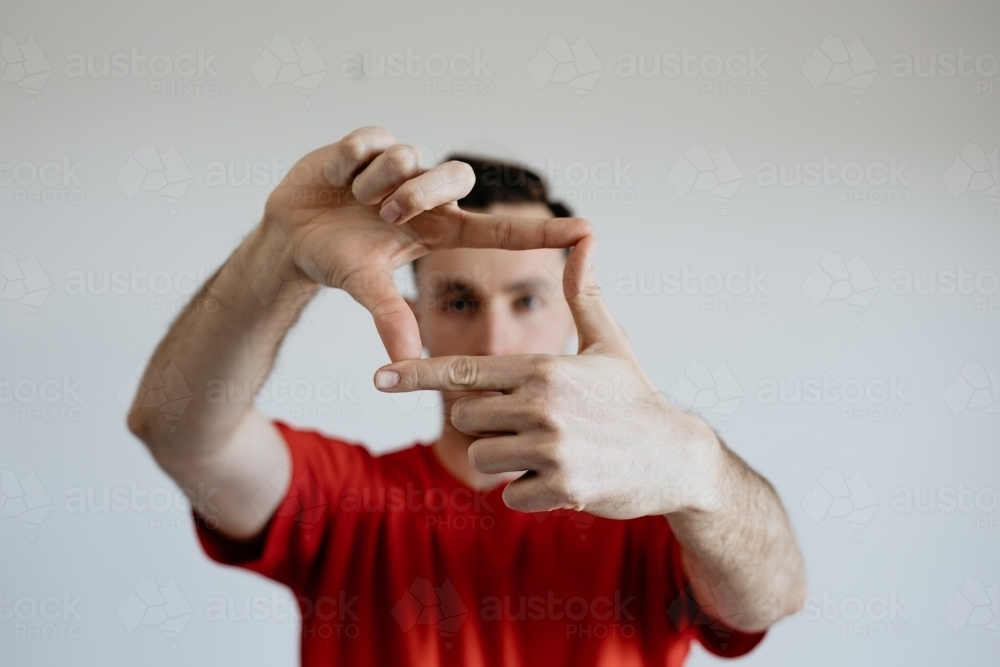 Young man, eyes looking through fingers that make a square - Australian Stock Image