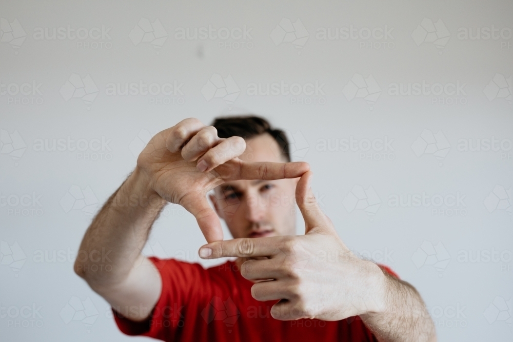 Young man, face looking through fingers that make a square - Australian Stock Image