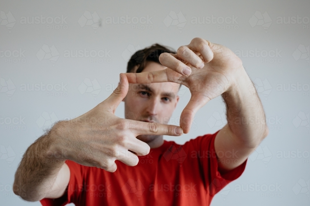 Young man, face looking through fingers that make a square - Australian Stock Image