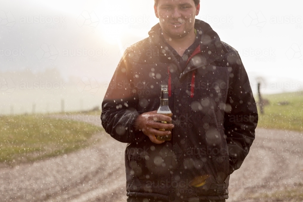 Young man having a beer in the rain - Australian Stock Image