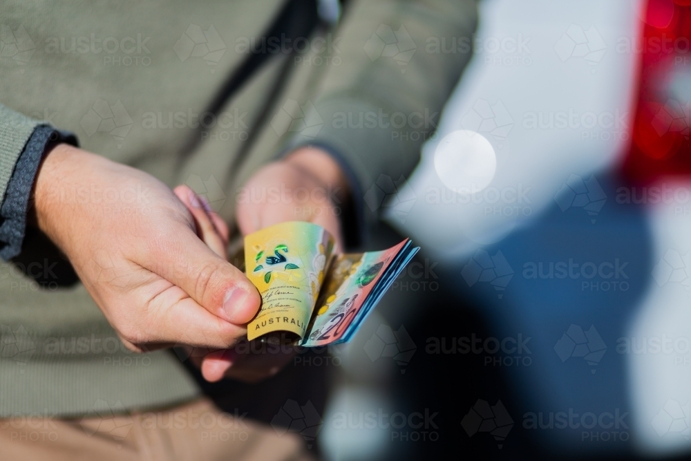 Young man holding cash standing in front of car paying up front - Australian Stock Image