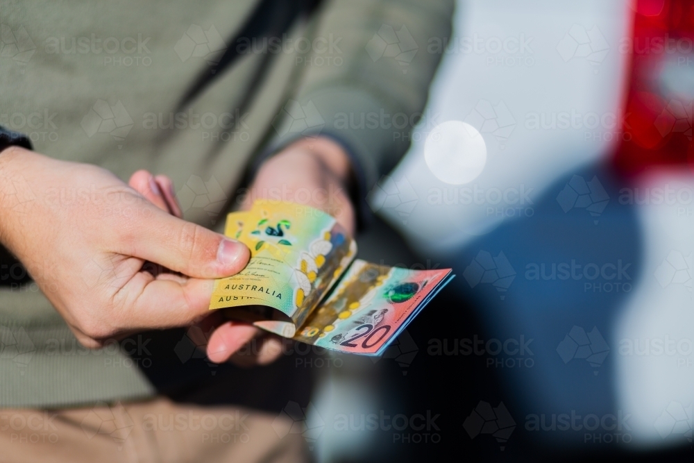 Young man holding cash standing in front of car paying up front - Australian Stock Image