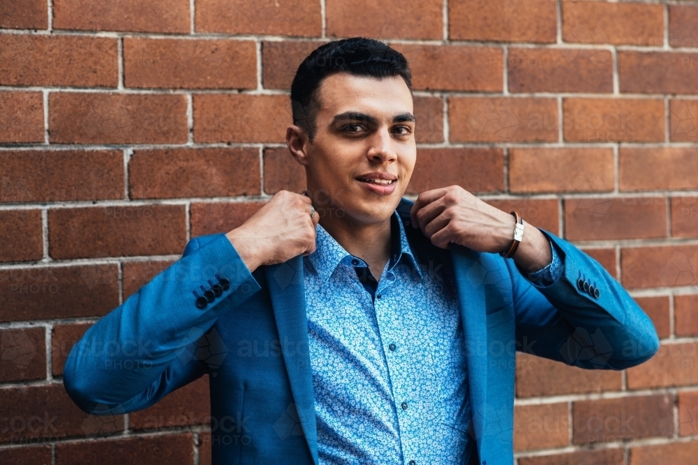 young man in blue suit in front of brick wall - Australian Stock Image