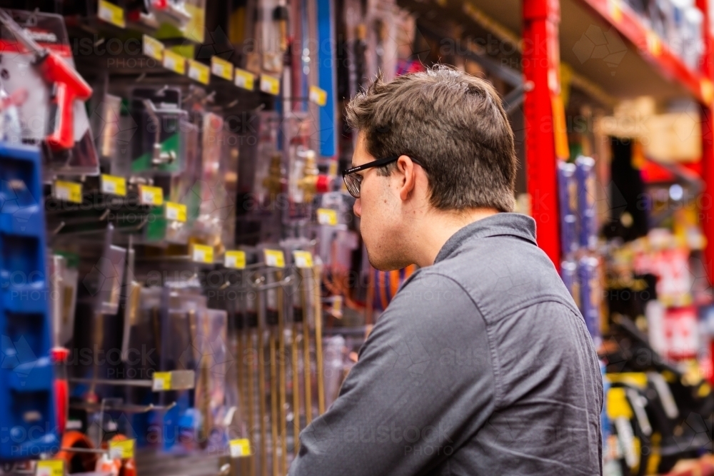 Image of Young man in hardware store looking at tools - Austockphoto