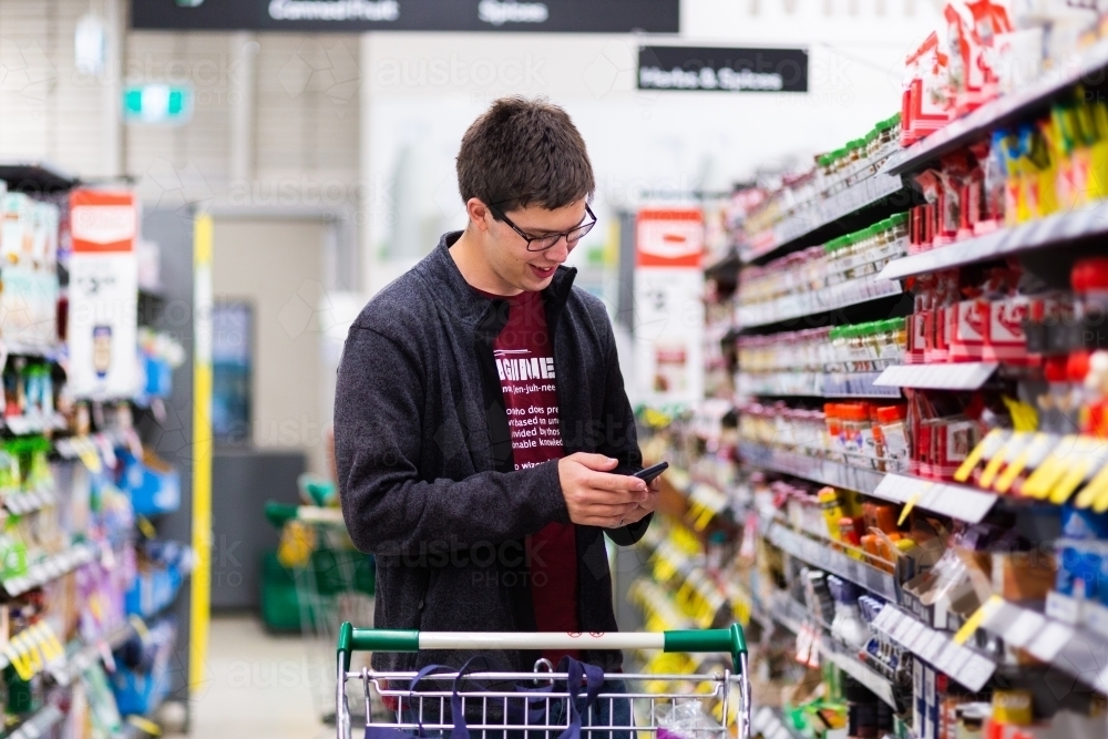 Young man in his 20s doing the family grocery shopping checking shopping list on his phone - Australian Stock Image