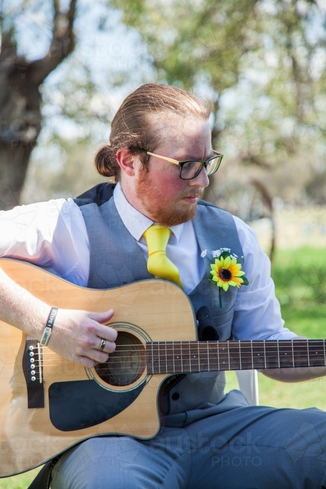 Young man in his 20s wearing a tie and playing guitar outside - Australian Stock Image