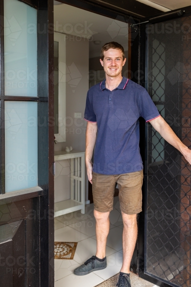 Young man in his twenties working as NDIS provider standing at front door welcoming into home - Australian Stock Image