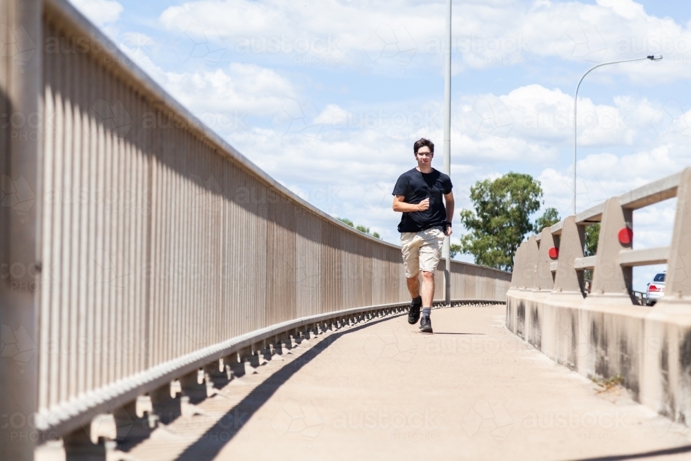 young man jogging over bridge on footpath - Australian Stock Image