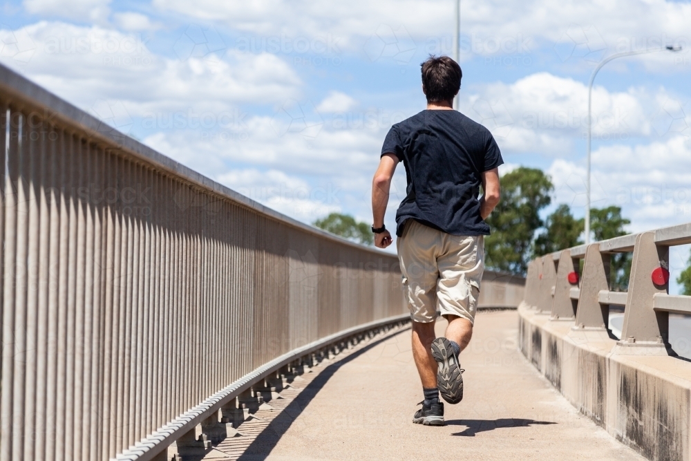 young man jogging over bridge on footpath - Australian Stock Image