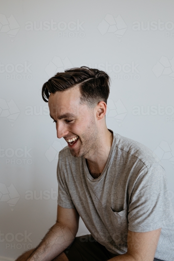 Young man laughing grey shirt plain background - Australian Stock Image