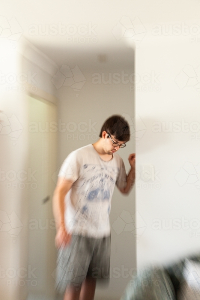 young man leaning on doorframe experiencing vertigo, spinning, dizziness - Australian Stock Image