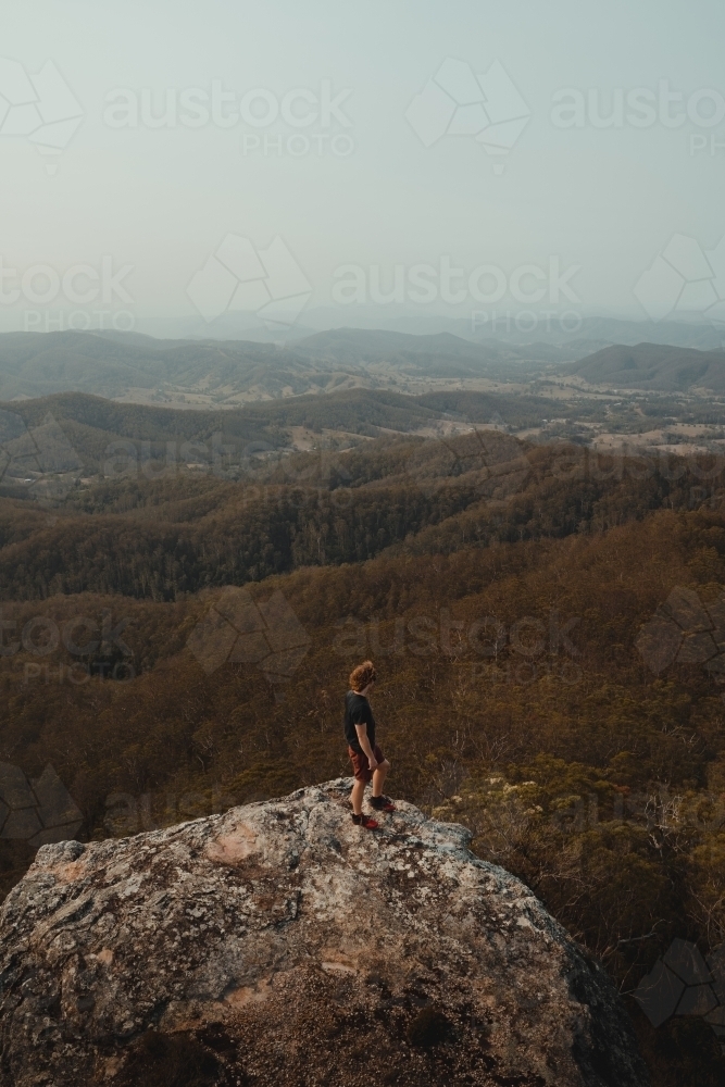 Young man on a mountain top looking at the views of the valley below. - Australian Stock Image