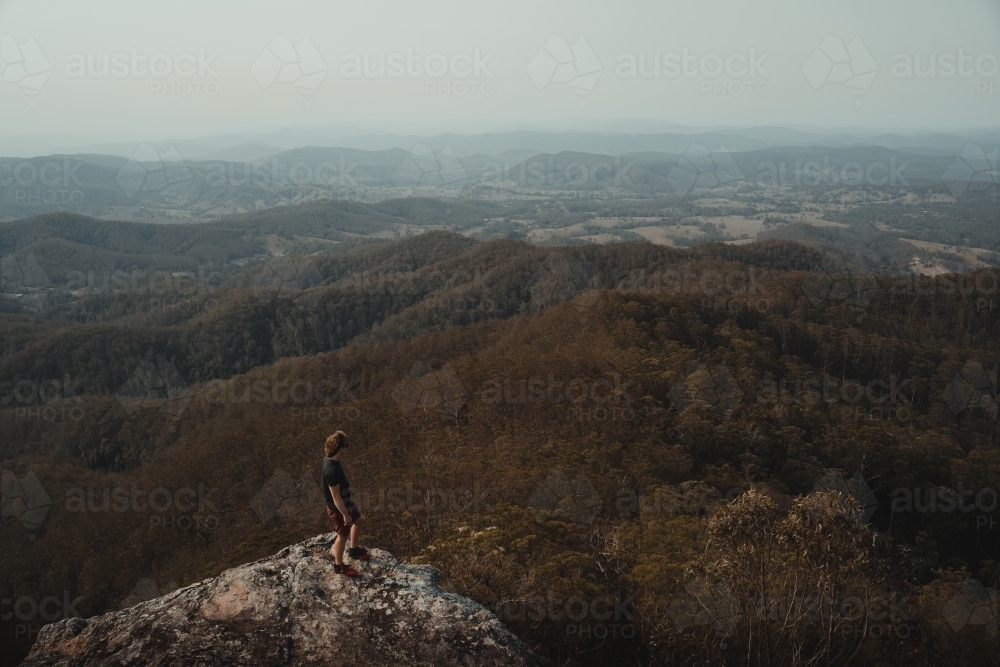 Young man on a mountain top looking at the views of the valley below. - Australian Stock Image