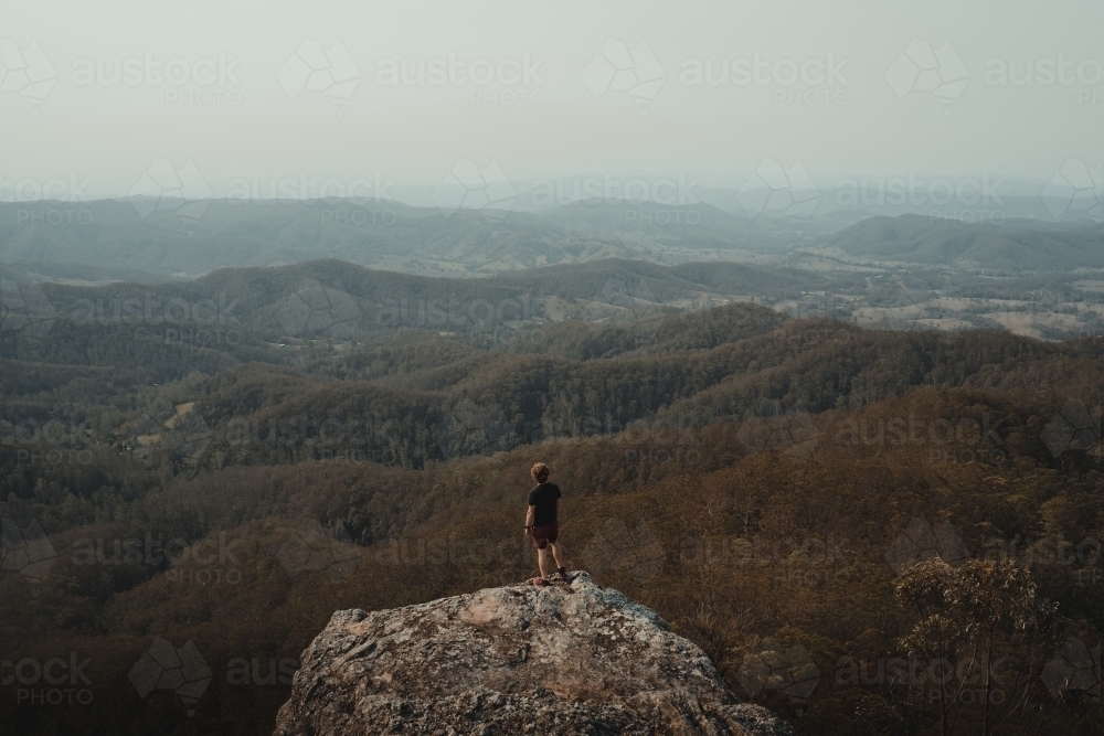 Young man on a mountain top looking at the views of the valley below. - Australian Stock Image