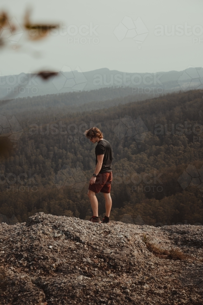 Young man on a mountain top looking at the views of the valley below. - Australian Stock Image