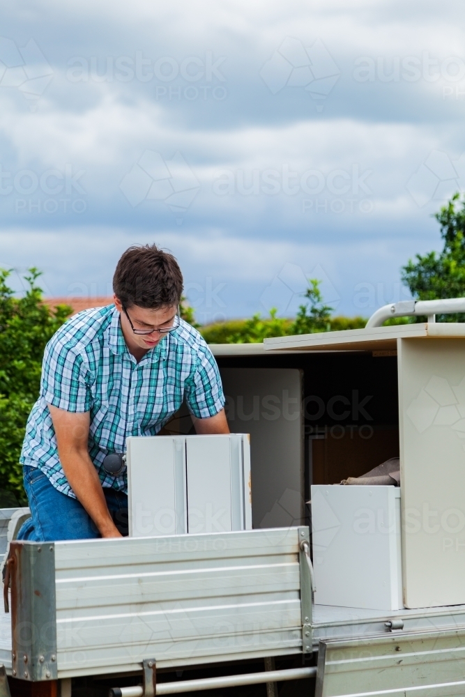 Young man packing office desk onto ute trailer, moving house - Australian Stock Image