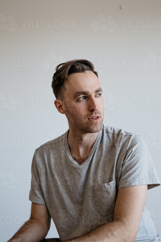 Young man pensive look grey shirt plain background - Australian Stock Image