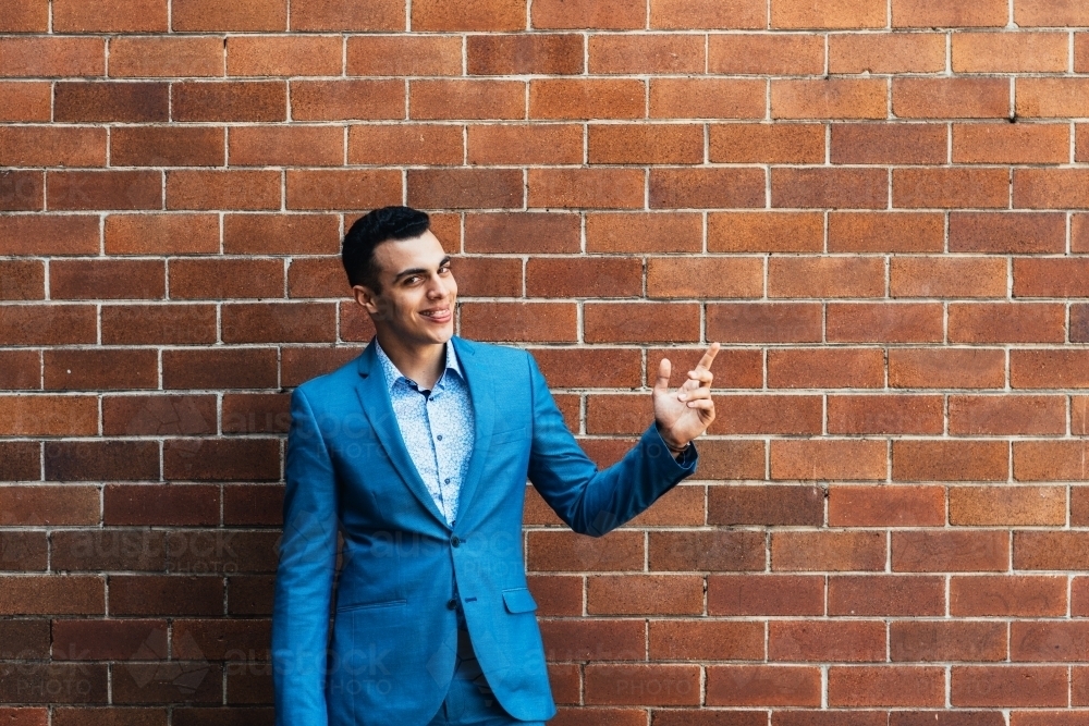 young man pointing, against a brick wall - Australian Stock Image