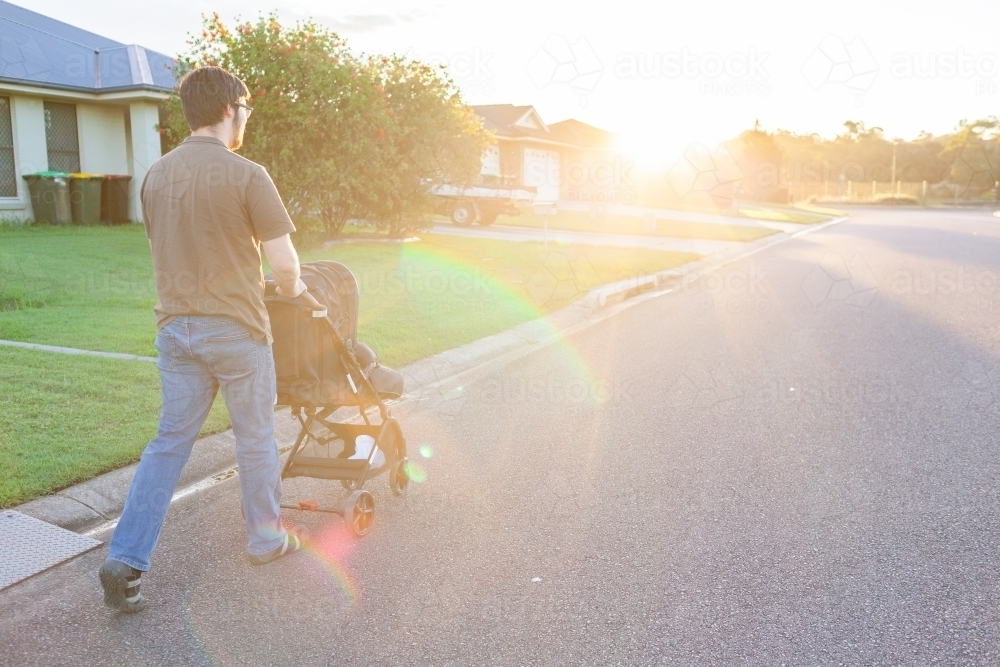 Young man pushing newborn in pram down urban street - Australian Stock Image