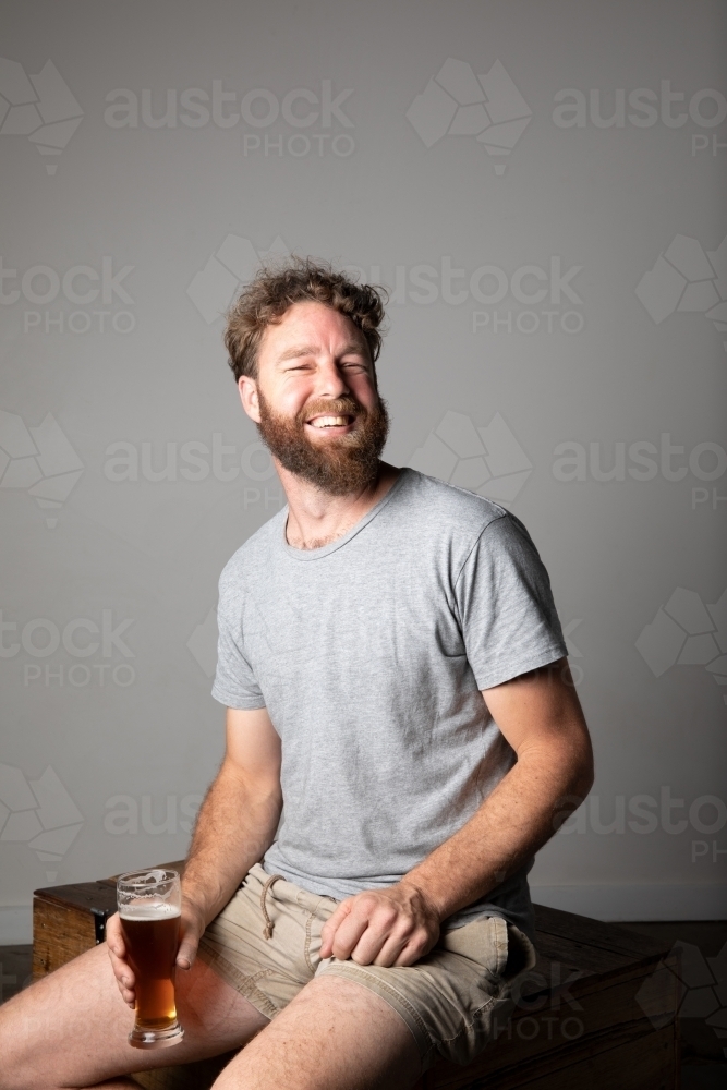Young man sitting, holding a glass of beer, relaxed and happy - Australian Stock Image