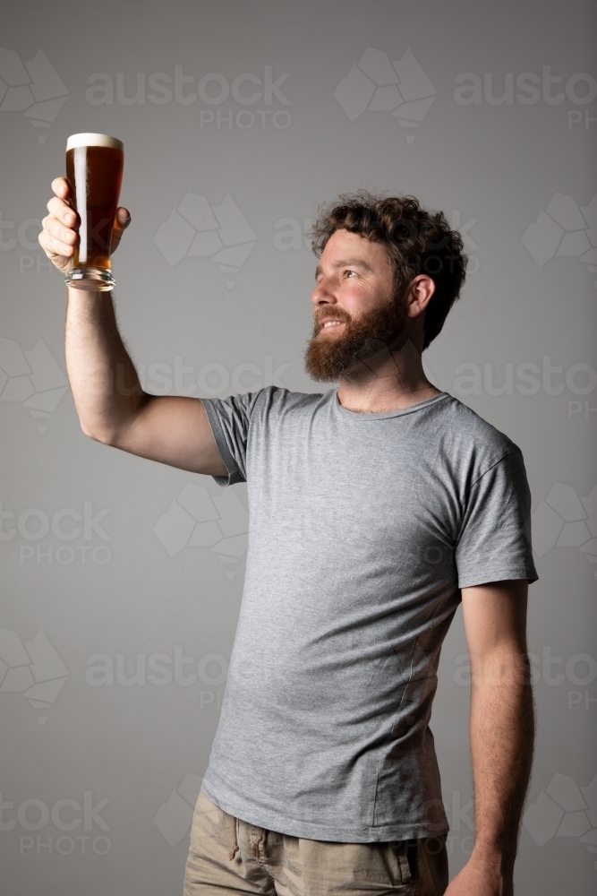 Young man sitting, holding a glass of beer, relaxed and happy - Australian Stock Image