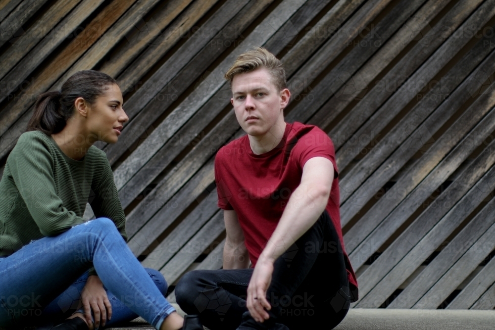 Young man sitting with female friend and looking at camera - Australian Stock Image