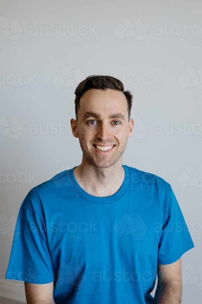 Young man smiling blue shirt plain background - Australian Stock Image