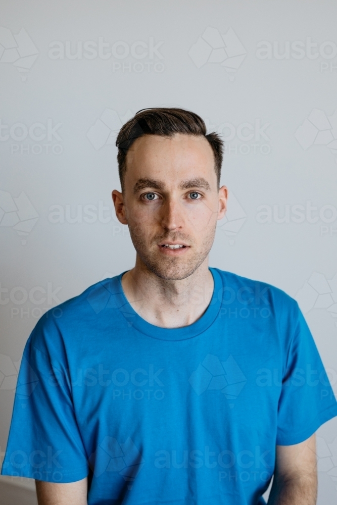 Young man smiling blue shirt plain background - Australian Stock Image