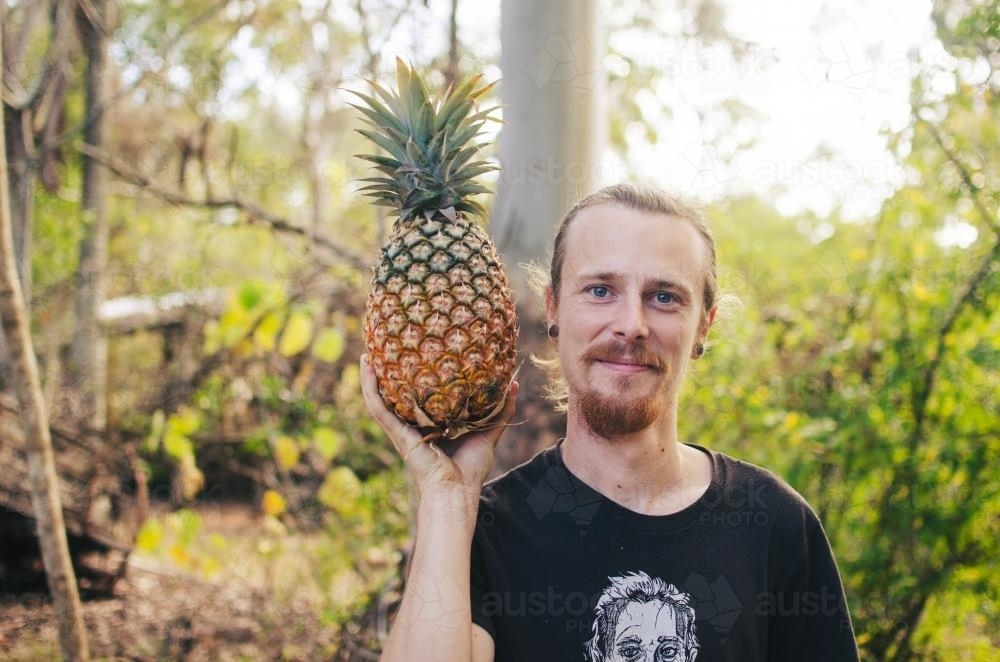 Young man smiling with a pineapple in the bush - Australian Stock Image