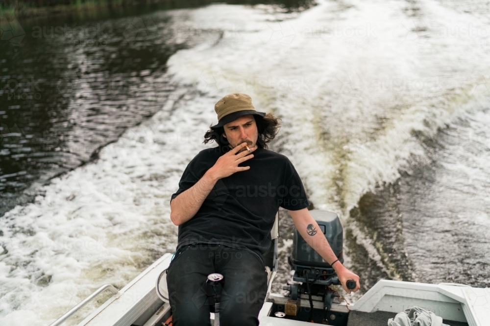Young Man Smoking at the Tiller of a Small Boat - Australian Stock Image