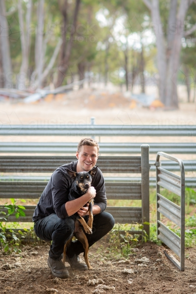 Young man squatting down with kelpie dog - Australian Stock Image