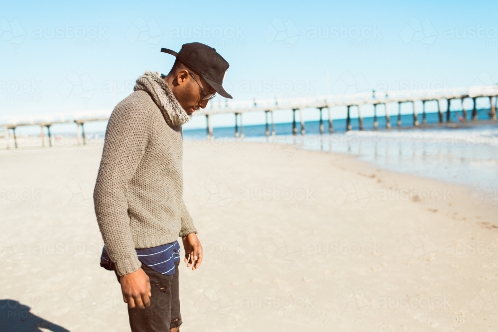 Young man standing on the beach looking down - Australian Stock Image